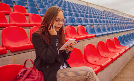 Female journalist speaking on smartphone, discussing competitions at street stadium.