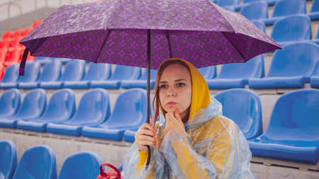 Pensive lady with umbrella touching chin and looking away on tribuneの写真素材