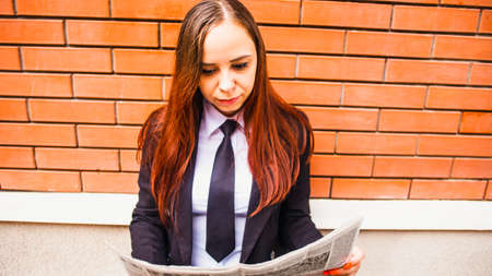 Young woman reading newspaper on street. Lady with long hair in casual clothes standing on the street and reading newspaper.の写真素材