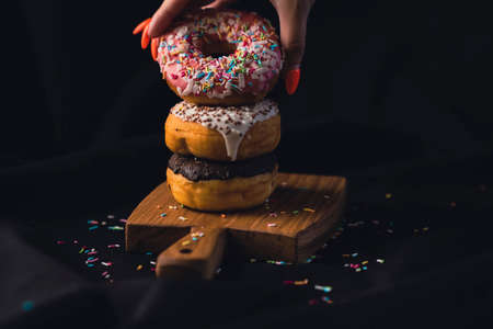 Close-up of a woman's hand taking a delicious donut from a wooden board. Delicious donuts laid out on a wooden cutting board on a black background.の写真素材