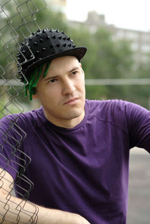 Young man with green dreadlocks in black cap, purple t-shirt posing through hole of lattice fenceの写真素材