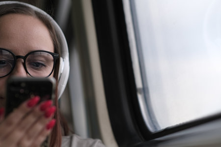 Portrait of young woman in glasses browsing mobile phone, riding on train. close up. Pretty female...