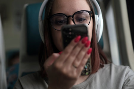 Portrait of young woman in glasses browsing mobile phone, riding on train. close up. Pretty female...