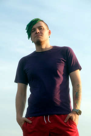 Portrait of young man with green dreadlocks posing on background of cloudy sky