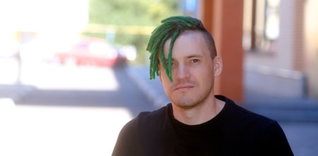 Young handsome man with green dreadlocks in black t-shirt posing on city streetの写真素材