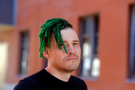 Young handsome man with green dreadlocks in black t-shirt posing on city street