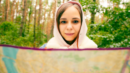 Cute girl reading map in forest. Traveling woman with backpack with open map in woods