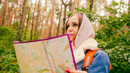 Cute girl reading map in forest. Traveling woman with backpack with open map in woodsの写真素材