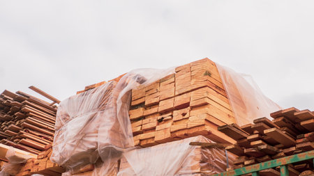 Fresh wooden boards in polypropylene packaging on the background of cloudy sky. Stack of industrial natural timber building materials on building siteの写真素材