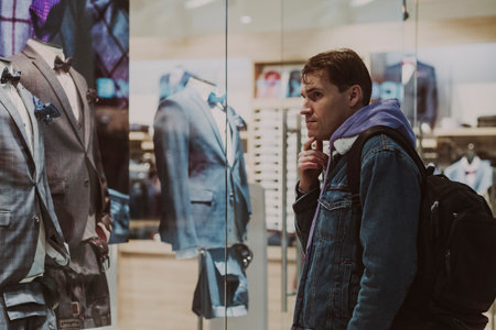 Portrait of young thoughtful man considering showcase in shopping center. Concept of shopping, dream, desireの写真素材