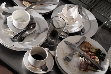 Dirty plates and glasses after a meal in the kitchen in the restaurant. Heap or pile of unclean glass and plates of breakfast or lunch tableの写真素材
