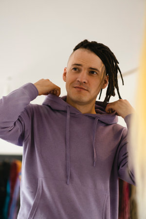 Young man looking in mirror, considering his new dreadlocks. Handsome guy preening in front of...
