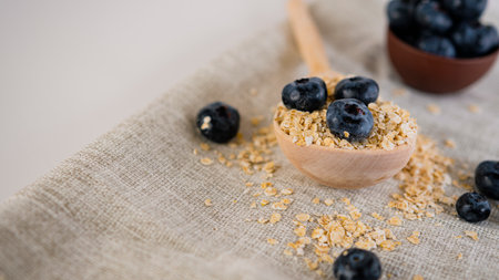 Oat flakes in large wooden spoon with blueberry on napkin on white backgroundの写真素材