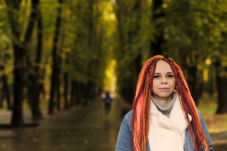 Portrait of young woman with ginger dreadlocks posing in forest park. Pretty female with bright...