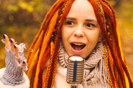 Young woman with bright hairstyle with retro microphone in autumn forest. Portrait of female singer...