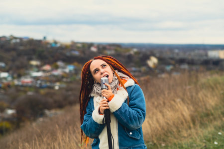 Young woman with dreadlocks singing into microphone in countryside. Female singer enjoying singing in natureの写真素材