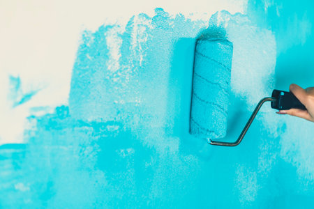 Unrecognizable person applying blue paint on wall. Female hand with roller painting wall. Concept of repair work and improvement of housing conditionsの写真素材