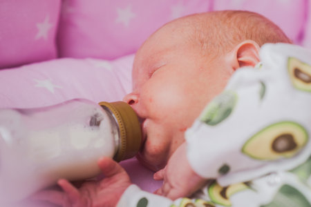 A newborn baby independently drinks milk or a dry mixture from a bottle, at homeの写真素材