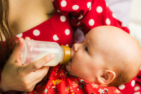 Young mother feeding her baby with a bottle of milk on the bedの写真素材