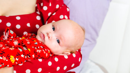 Newborn baby girl in red polka dot dress on white background