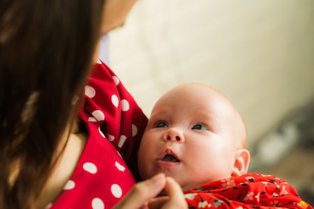 Newborn baby girl with mother in red dress in the kitchen.