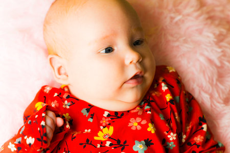 Newborn baby girl in red dress on pink background. Close up.