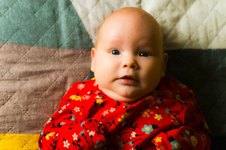 Portrait of a cute little baby girl in red dress on the bed
