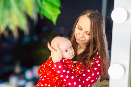 Young mother holding her newborn baby in hands and looking in the mirror