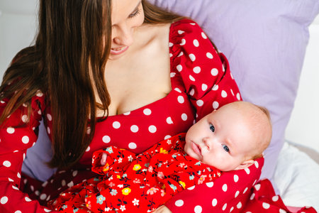 Mother with her newborn baby in a red dress on a white background