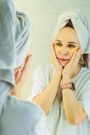 Beautiful woman applying collagen patches under eyes in front of the mirror.の写真素材