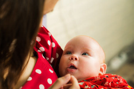 Young mother with her newborn baby in a red dress at home.