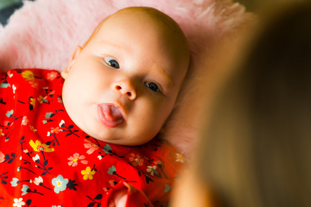 Newborn baby girl in red dress lying on mother's lap.