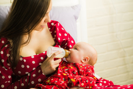 Young mother feeding her baby with milk in bed at home in the morningのeditorial素材
