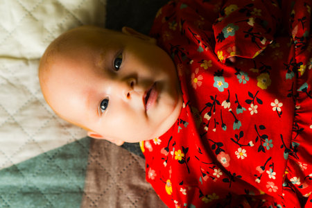 Cute baby girl in a red dress lying on the bed.のeditorial素材
