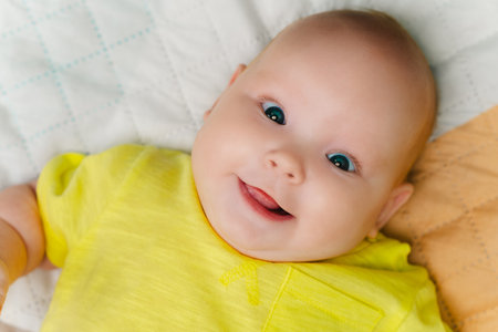 Portrait of a cute newborn girl lying on a bed in a yellow T-shirtの写真素材