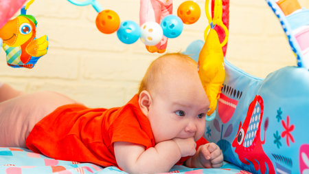A close-up portrait of a cute adorable newborn baby with blue eyes licking his sucking fingers with a fist. The child is teething.の写真素材