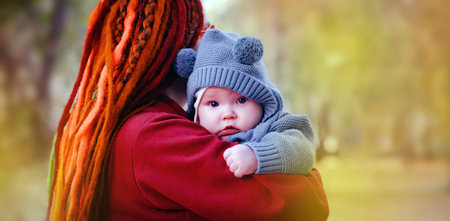 Cute little newborn baby in his mom's arms in the park. Autumn season
