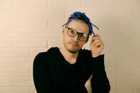 A man with bright purple dreadlocks and glasses twirls dreadlocks in his hand