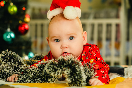 Newborn baby boy in a red Santa hat lies on the bed near the Christmas treeの写真素材