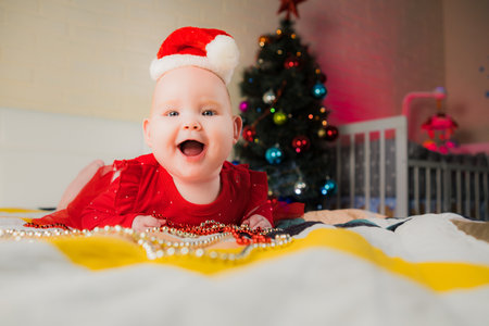 Little baby girl in Santa hat with Christmas tree in the background.の写真素材