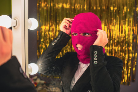 A young woman in a pink balaclava looks in the mirror.の写真素材