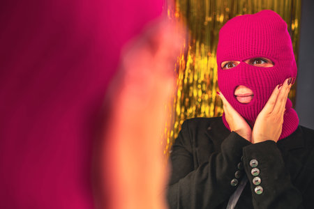 A young woman in a pink balaclava looks in the mirror.の写真素材