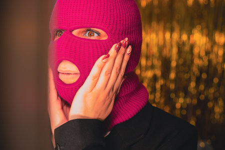 A young woman in a pink balaclava looks in the mirror.