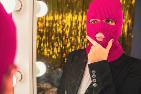 A young woman in a pink balaclava looks in the mirror.の写真素材