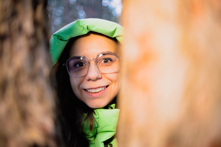 Portrait of a beautiful girl in a green jacket and glasses in a winter forest.の写真素材