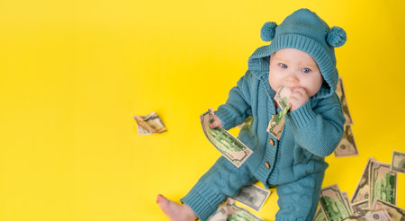 Baby in a blue knitted suit with money on a yellow background. Cute kid with dollars on a yellow...