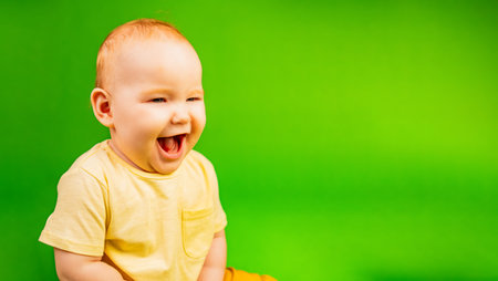 Laughing Baby in Yellow Clothing Against Vibrant Green Backgroundの写真素材