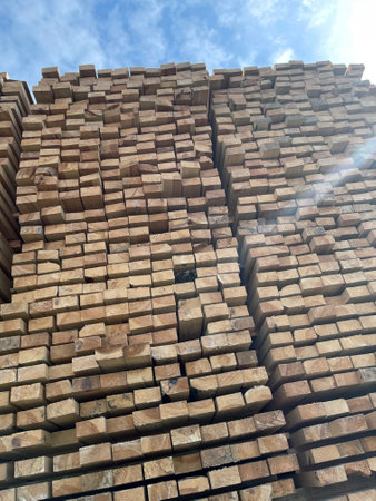 Stacked Timber Planks at a Lumberyard Awaiting Transportation. Stacked wooden planks in varying...