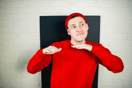 A man in a red hoodie and hat dances against a white brick wall.の写真素材