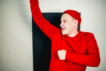 A man in a red hoodie and hat dances against a white brick wall.の写真素材